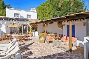 Un patio con mobiliario exterior, un toldo de paja y suelo de piedra.