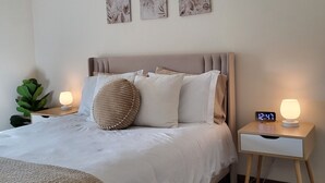 Ein Schlafzimmer mit einem Bett, Nachttischen, einem Beistelltisch mit Lampe und Wandbildern.