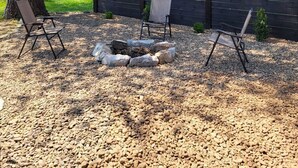 Eine Terrasse mit Feuerstelle, zwei Stühlen, einem Baum und einem Zaun.