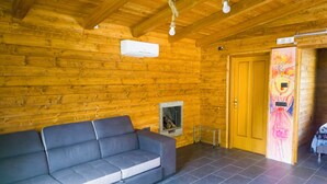 A log cabin interior with a grey sofa, a fireplace, and a wooden door. - Secret Garden (Grottolella)