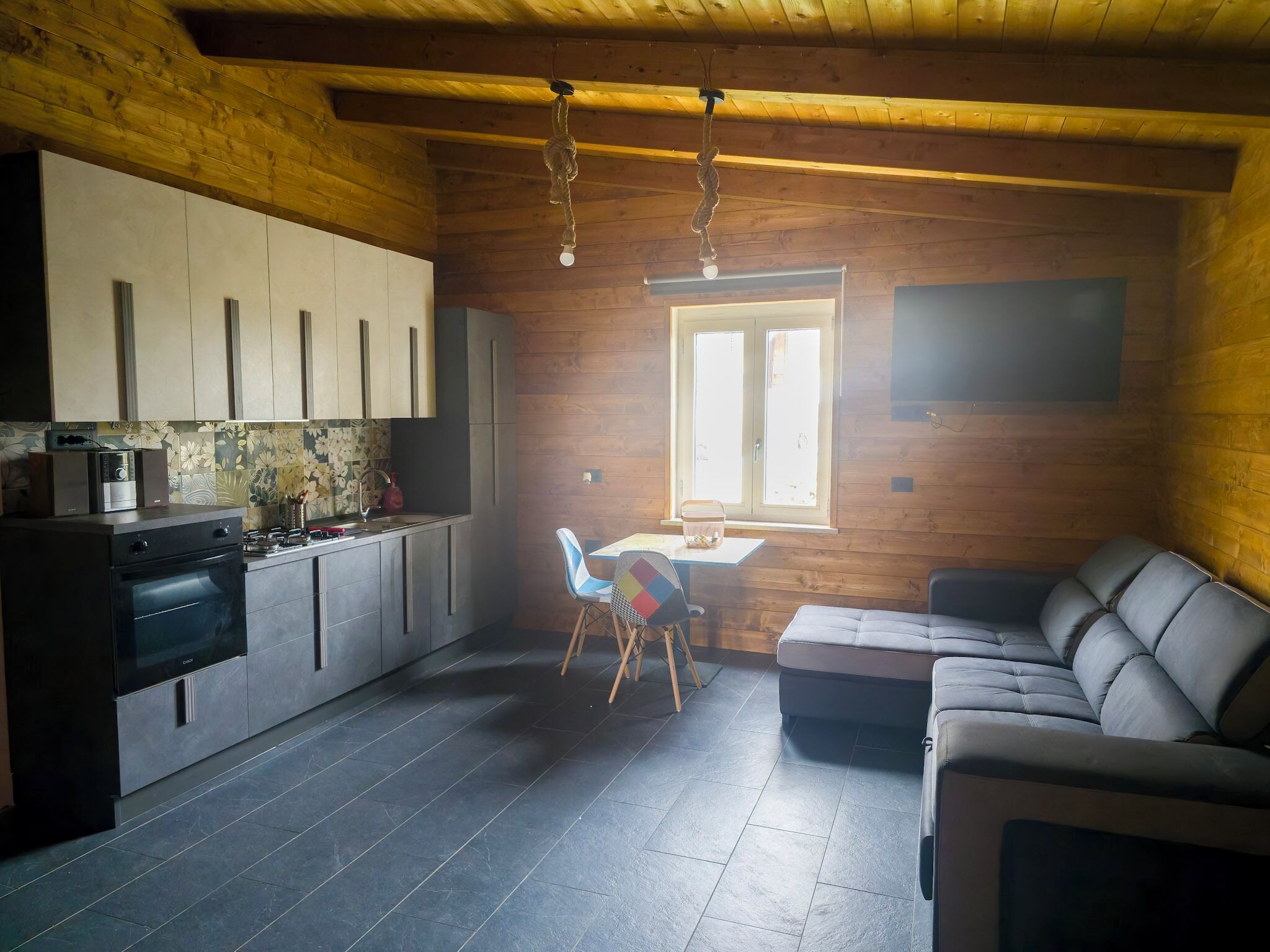 Cozinha moderna com armários escuros, forno embutido e área de jantar com mesa e cadeiras.