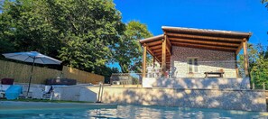 A poolside area with a covered seating area, stone walls, and a clear blue sky. - Secret Garden (Grottolella)