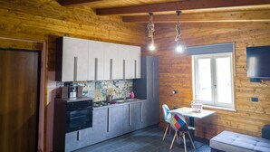 A kitchen with wooden walls, a tiled backsplash, and modern cabinetry. There is a dining area with a table and chairs, and a television mounted on the wall. - Secret Garden (Grottolella)