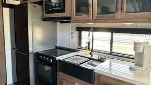 Une cuisine de taille réduite, dotée de meubles en bois, d’un réfrigérateur noir, d’une cuisinière et d’un four à micro-ondes.