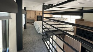 Un intérieur de camping-car compact comprenant un lit superposé, un coin cuisine et une fenêtre laissant entrer la lumière naturelle.