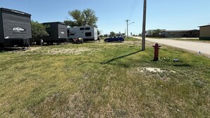 A grassy area with a red fire hydrant, a trailer, and a car parked nearby. - Grasshopper Flats RV Pad (Interior)