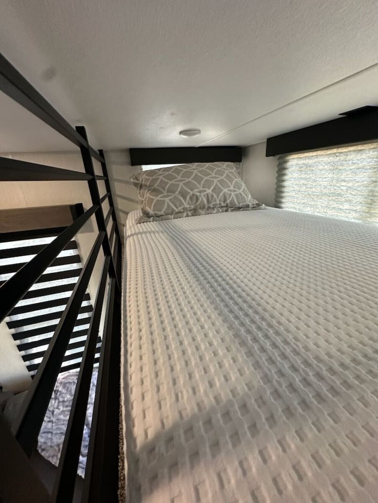 Een stapelbed met een kussen met een patroon en een matras met een geribbelde hoes.