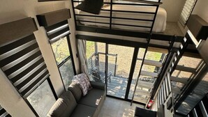 Ein modernes Interieur mit einer loftartigen Sitzgruppe, einer Treppe und großen Fenstern mit Blick ins Freie.