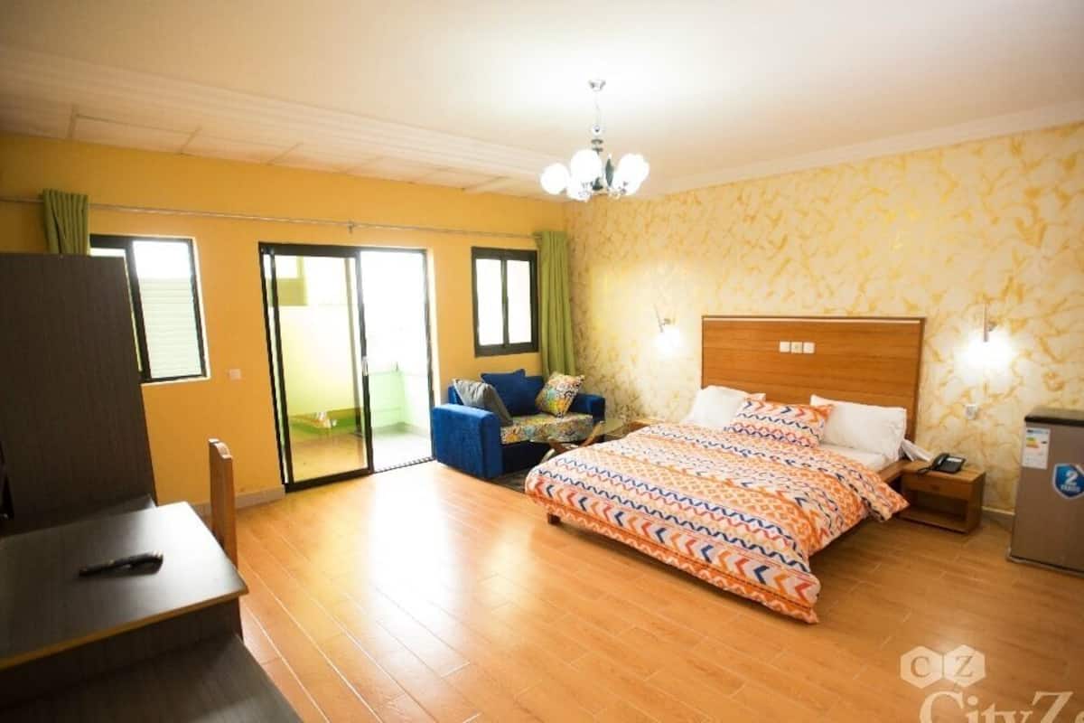 A hotel room with a bed, a desk, a chair, a TV, and a minibar.