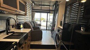 Une cuisine compacte équipée d’une cuisinière, d’un évier et d’un lave-linge, ainsi que d’un canapé et d’une vue sur l’extérieur.