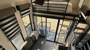 Un intérieur moderne avec un espace salon aménagé dans un style industriel, un escalier et de grandes fenêtres offrant une vue sur l’extérieur.