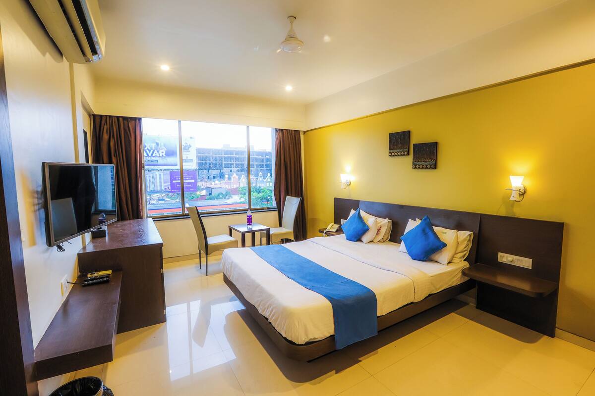 A hotel room with a bed, bedside table, TV, and a view of the outside.