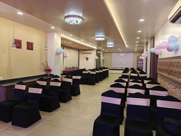 Un salón de banquetes con filas de sillas, un escenario y una pantalla de proyector.