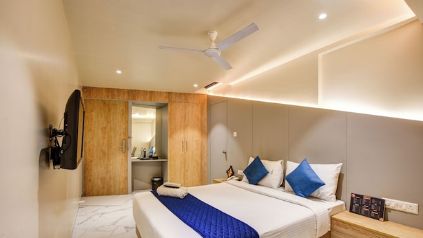 Ein modernes Hotelzimmer mit einem großen Bett, einem Deckenventilator, einem Holzschrank, einem Nachttisch und einem an der Wand montierten Fernseher.