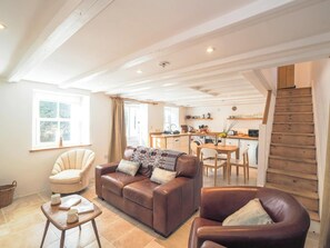 Un salon chaleureux avec un canapé, un fauteuil et une table basse, une cuisine dotée de meubles en bois et d  ’appareils électroménagers, et un escalier menant à un autre niveau.