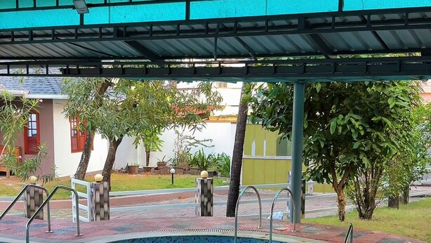 A swimming pool with a tiled edge, a covered area with a metal roof, and a wooden deck. - Invito Beach Resort – A Bright, Beautiful Arabian Sea Stay (Kannur)