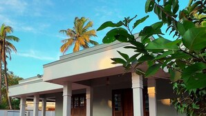 A two-story building with a covered entrance and a red and black tiled walkway. - Invito Beach Resort – A Bright, Beautiful Arabian Sea Stay (Kannur)