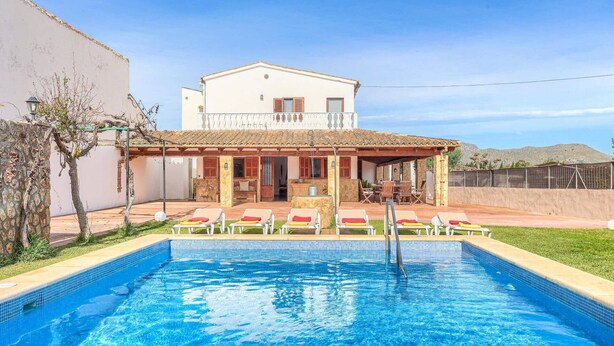 Una casa con piscina, un patio con sillas y una montaña al fondo.