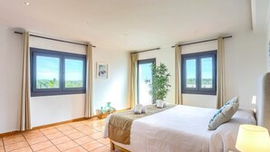 Un dormitorio con una cama, una planta en maceta y vistas a través de las ventanas.