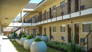 A modern hotel with a covered walkway, large planters with greenery, and a second-floor balcony. - Lemon Heights Inn (Tustin)