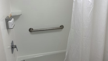Un baño con una bañera blanca, un cabezal de ducha, una barra de apoyo, un perchero para toallas y una cortina de ducha blanca.