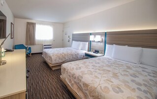 Habitación de hotel con dos camas, un escritorio, una silla, una ventana con cortinas, un equipo de aire acondicionado y una lámpara de pared.