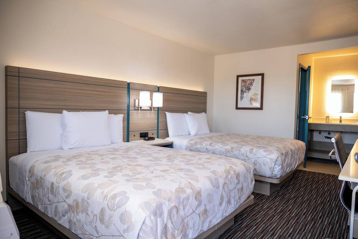 Une chambre d’hôtel avec deux lits, une table de chevet, une salle de bain avec un miroir et un tableau encadré au mur.