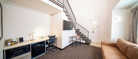 A modern hotel room with a kitchenette, a dining area, a staircase, and a living room with a sofa.