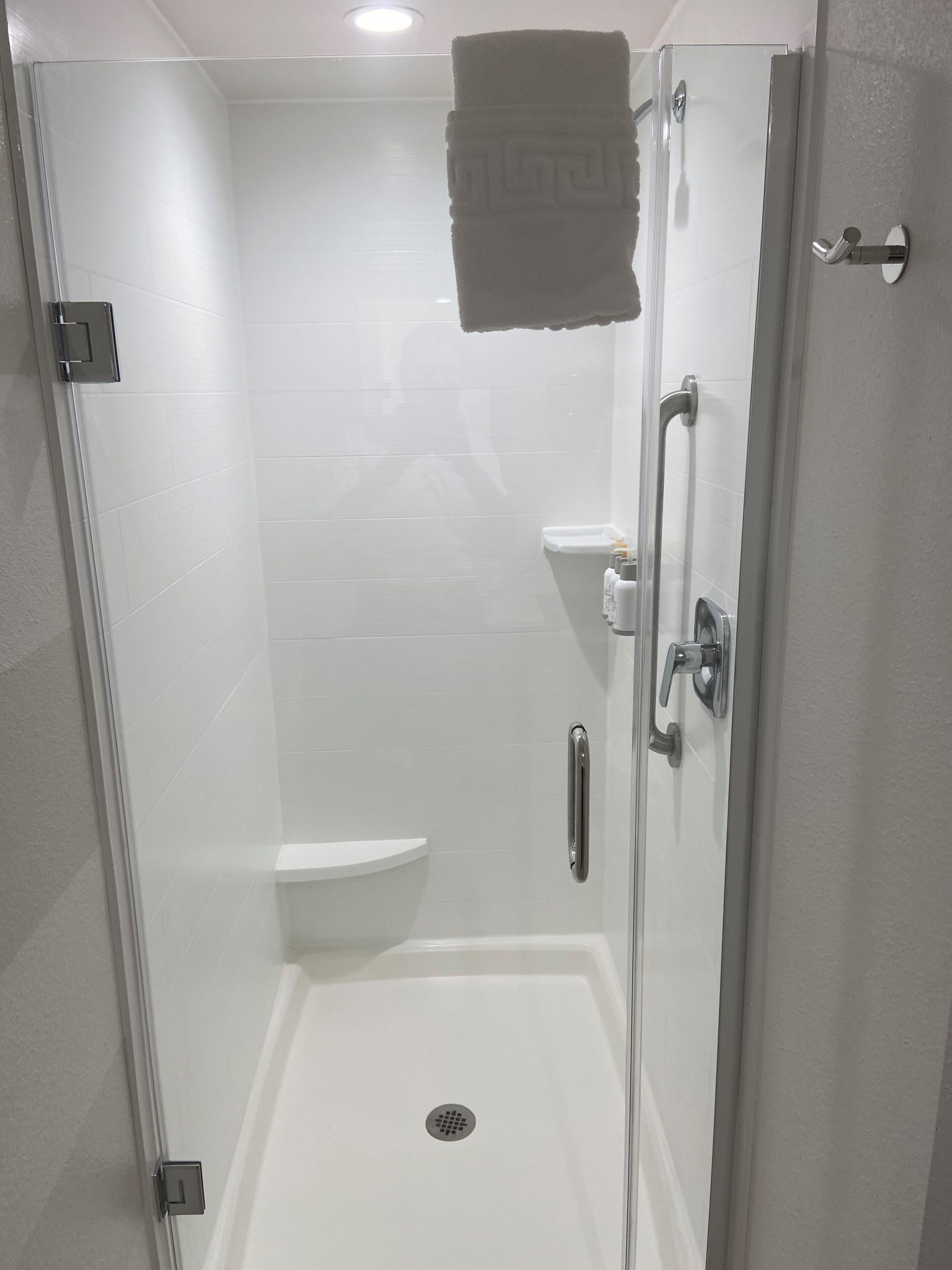 Une cabine de douche fermée par des parois de verre, avec un mur recouvert de carreaux blancs, une douchette à main et une serviette accrochée à la porte.