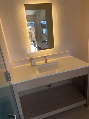 A bathroom with a white sink, a mirror above it, and a visible shower area. - Lemon Heights Inn (Tustin)