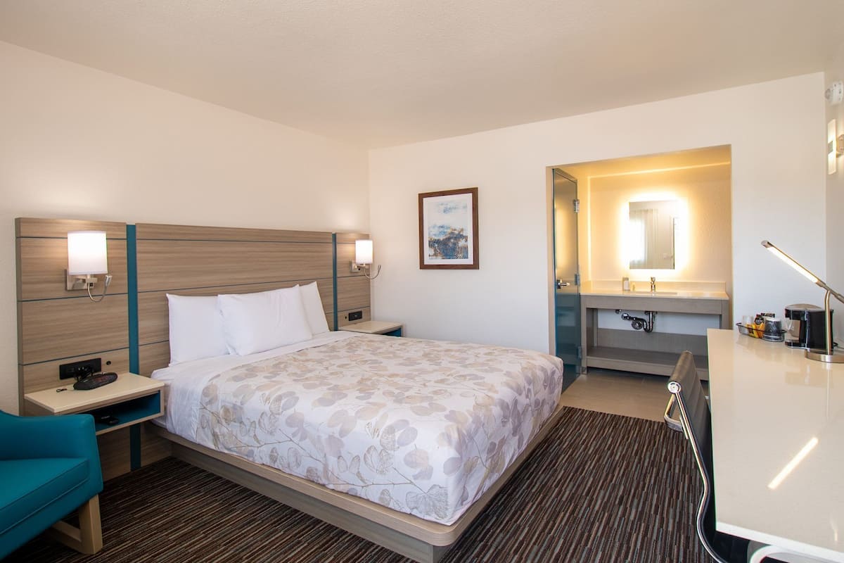 Une chambre d’hôtel comprenant un lit, une table de chevet, une lampe et un petit bureau avec une chaise.