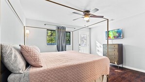 A bedroom with a bed, a ceiling fan, a dresser, a TV, and a window with curtains. - Spacious 4-bedroom house in welcoming San Antonio near trails, Pearl, Gardens (San Antonio)