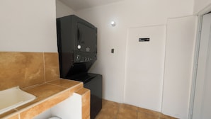 Una cocina compacta con lavadora y secadora integradas, una puerta blanca con un cartel de 'No Smoking' y un salpicadero de azulejos.