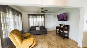 A living room with a sofa, a yellow armchair, a ceiling fan, and a TV on the wall. - Loma Bella/ Private Villa for 14 near beach,2 homes  (Patillas)