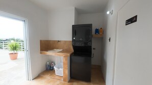 Una kitchenette compacta con un lavamanos, un refrigerador negro y un estante pequeño con botellas.