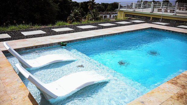 Una piscina rectangular con dos sillones blancos y una pequeña zona de hidromasaje.