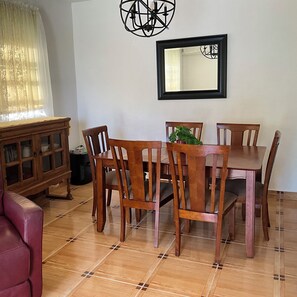 Un comedor con mesa y sillas de madera, un armario, un espejo y una planta en maceta.