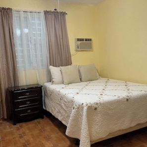 Un dormitorio con cama, cómoda, cortinas y aire acondicionado.