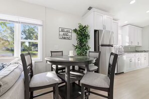 Een moderne keuken met witte kasten, een roestvrijstalen koelkast en een eethoek met een ronde tafel en vier stoelen.