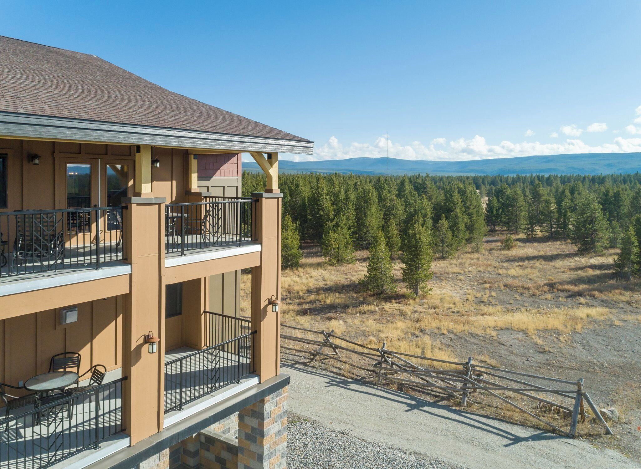 A two-story building with a balcony, outdoor seating, and a view of a forest and mountains.