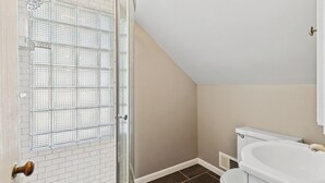 A bathroom with a glass shower door, a white toilet, and a beige wall. - Beautiful 3-bedroom house with AC in adorable Des Moines (Des Moines)