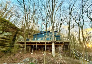 Eine Holzterrasse mit einem blauen Gebäude auf Stelzen, umgeben von Bäumen.