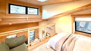 A high-ceilinged room with a skylight, a bed, a view of trees, and a balcony with a railing.