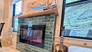 A fireplace with a stone surround, a guitar leaning against the wall, and a window with a view of a rocky landscape.
