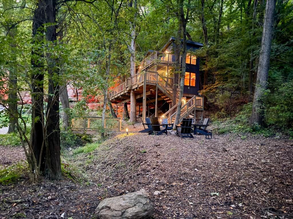 Una cabaña con terraza de madera y zona de estar al aire libre rodeada de árboles.
