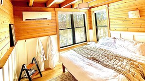 Ein Schlafzimmer einer Holzhütte mit einem Bett, einem Fenster, einer Heizung und einem kleinen Tisch mit Stuhl.