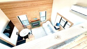 Une pièce aux hauts plafonds, avec des murs en bois, une cheminée, un canapé, une table et une fenêtre.