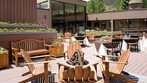 Un patio al aire libre con mobiliario de madera, incluyendo sillas tipo Adirondack y mesas, además de un brasero.