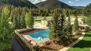 Ein Resort mit Schwimmbad, umgeben von Bäumen, einem Tennisplatz und einem Berg im Hintergrund.