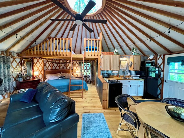 A yurt interior with a bunk bed, a dining area, kitchen, and a ceiling fan.